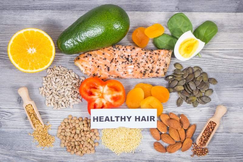 Nutrient-rich foods for healthy hair growth including salmon, avocado, eggs, almonds, seeds, citrus fruits, and leafy greens that help reduce hair fall and strengthen hair follicles